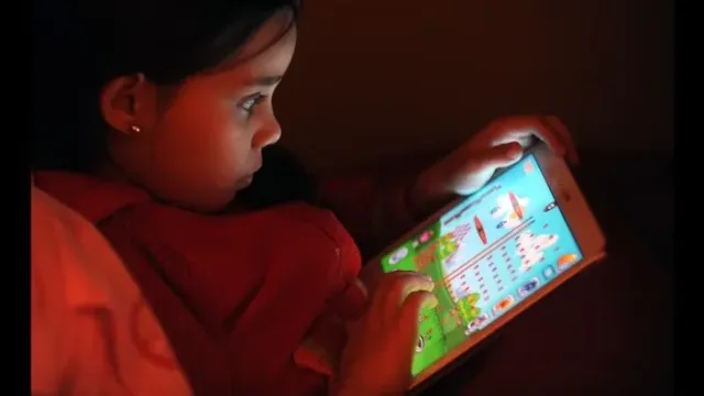 Niña pequeña de noche absorta en una tablet, con la cara iluminada por la pantalla