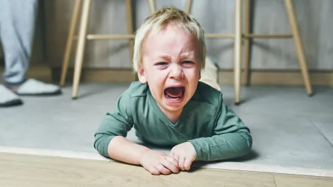 Niño pequeño en plena pataleta, llorando tirado en el piso de la casa